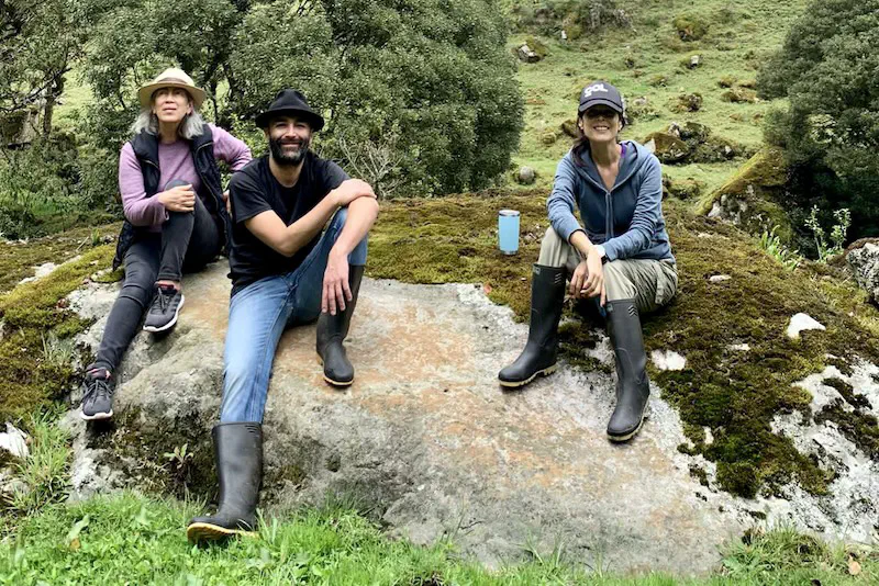 Three people sitting on a rock in a mountainous landscape.